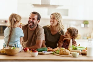 Cheerful parents having fun with their kids while preparing a healthy meal in the kitchen. Focus is on father.