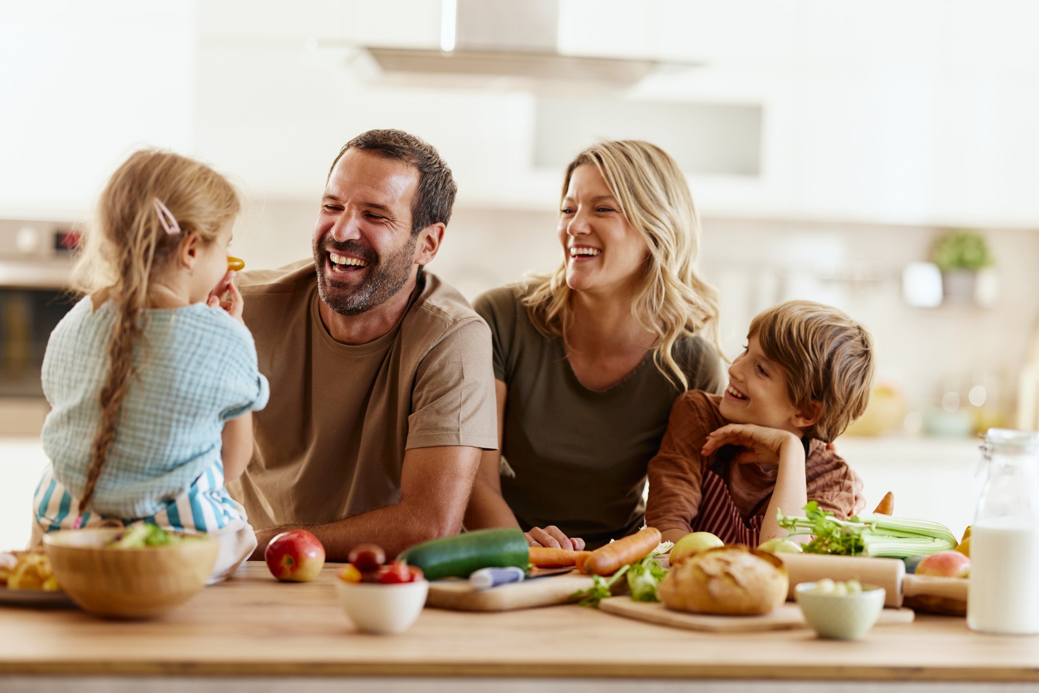 Cheerful parents having fun with their kids while preparing a healthy meal in the kitchen. Focus is on father.